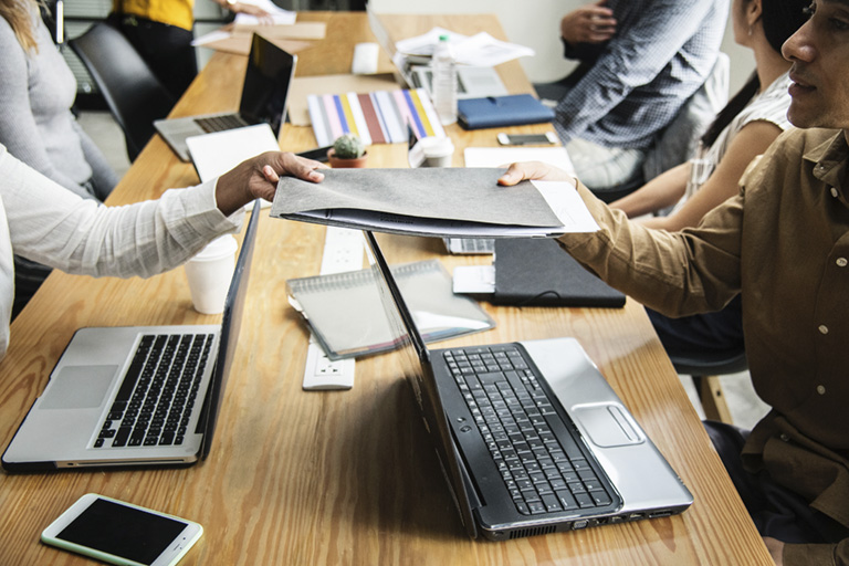 Menschen sitzen am Tisch mit Laptops, Handys, Kalender und Mappen